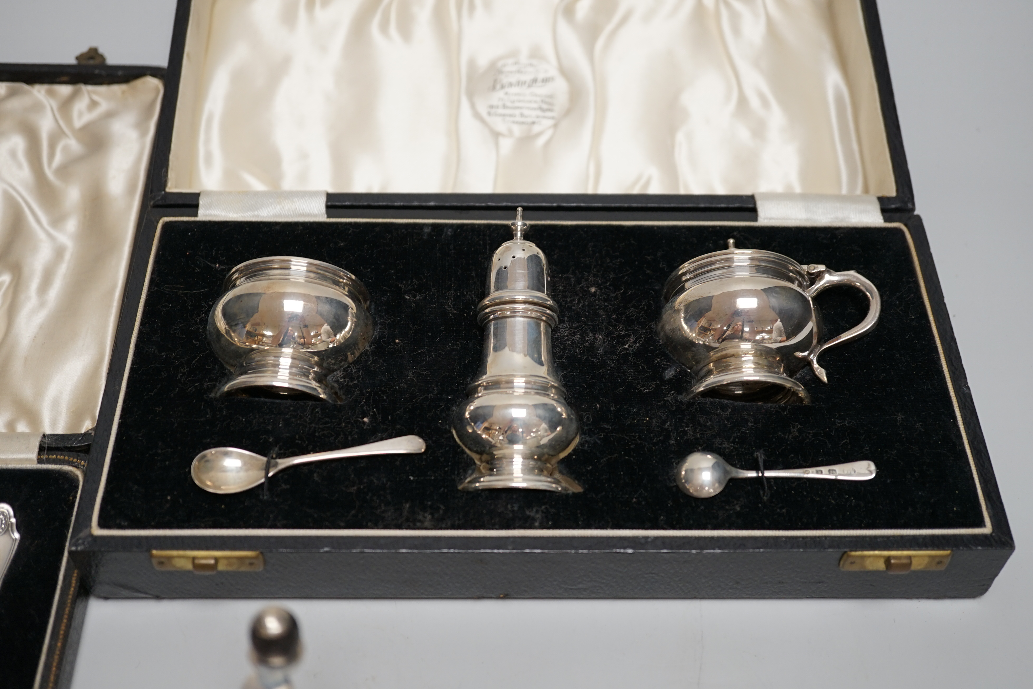 A cased George V silver three piece condiment set with two spoons, London, 1935, a cased set of six silver grapefruit spoons, a silver mounted glass pepper grinder and a white metal mounted glass match strike.